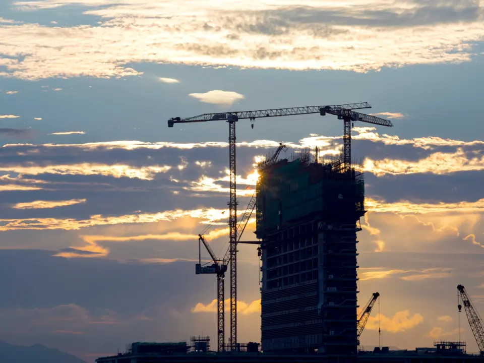 A building under construction with tower cranes at dusk